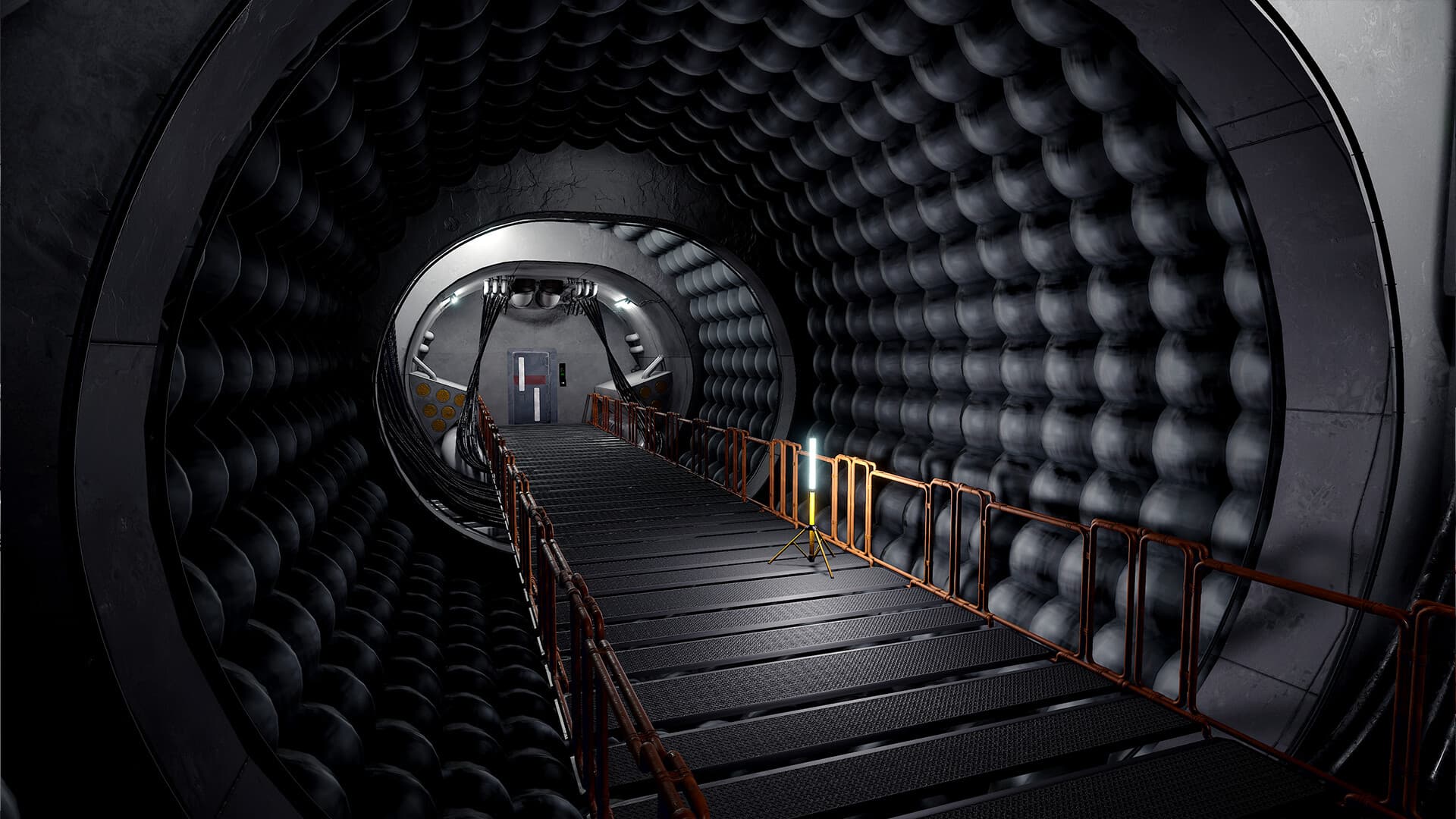 A cylindrical industrial tunnel with padded walls, orange railings and a lit metal walkway.